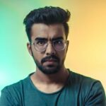A thoughtful adult man with eyeglasses posing for a portrait with a vibrant backdrop.